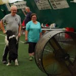 Man, woman, and border collie in front of industrial fan