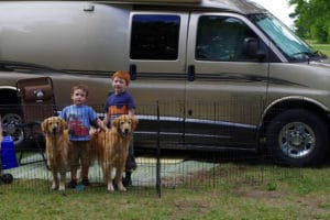 Two young boys, two Golden Retrievers in xpen around RV