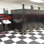 4 black restrooms stalls with white and black checked floor, white sinks