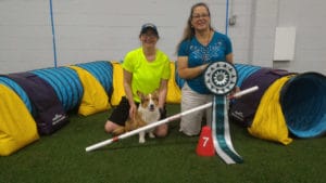 MACH7 bar and huge ribbon with Jo Powers, her Corgi Bug, and Judge Jacqui O'Neill, posed in front of agility tunnel