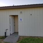 Small restroom building with "Cowgirls" sign at easy up tents and dog crates along side of agility ring at East Idaho Fairgrounds-BlackfootID