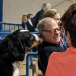 Tri-colored dog sniffing a man's ear. Man has half-smile, half-irritted expression. At MTSU Livestock Center, Murfreesboro TN