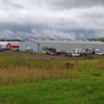 Wide shot of RVs parked beside building showing several other buildings behind the main one at South St. Louis County Fairgrounds, Dirt Floor Arena, Proctor MN