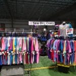 Sew Dog Crazy vendor area with t-shirts on racks with embroidered equipment bags on a wall rack at Yellow Breeches Sports Center, New Cumberland PA